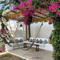 an outdoor seating area with pink flowers and greenery on the roof, along with a hammock