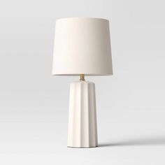 a white table lamp with a beige shade on the base and a light bulb attached to it