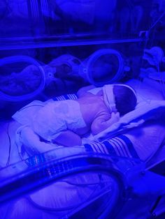 a baby in a hospital bed with blue light coming from the back and head lights on