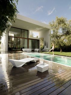 a woman standing in front of a swimming pool next to a white lounge chair on top of a wooden deck