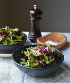 two black bowls filled with salad on top of a table