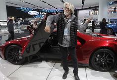 a man standing next to a red sports car in a showroom filled with people