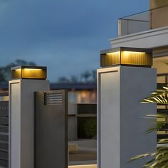 two lights on the side of a white building at night with palm tree in foreground