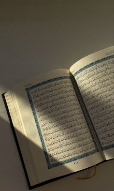 an open book sitting on top of a table next to a light shining through the window