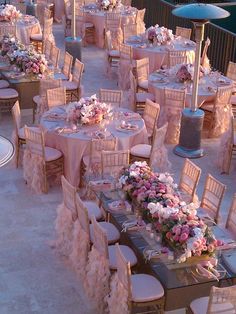 tables and chairs are set up for an outdoor wedding reception with pink flowers on them