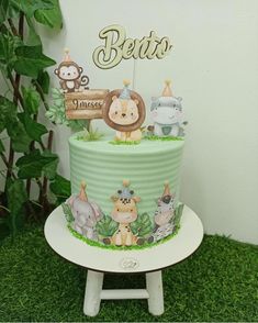 a green cake with animals on it sitting on top of a white stand in the grass