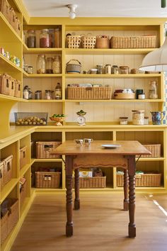 a kitchen with yellow shelving and lots of baskets on the shelf above the table