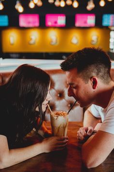 a man and woman sitting next to each other at a table drinking milkshakes