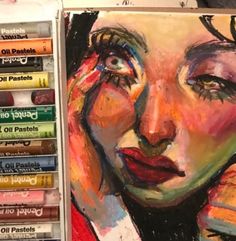 a painting of a woman's face with crayons in front of it