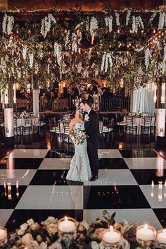 a bride and groom standing in front of candles on a checkered floor with flowers