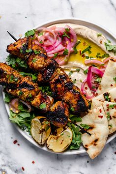 a white plate topped with chicken and veggies next to pita bread on top of a table