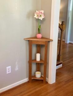 a small wooden table with a vase on top and candles in the corner next to it