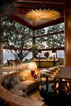 a living room filled with furniture and a fire place under a large ceiling fan on top of a wooden structure