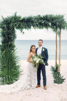 a bride and groom standing under an arch made out of palm trees on the beach