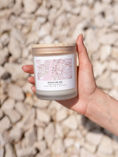 a hand holding a candle with a map on the front and inside, in front of some rocks