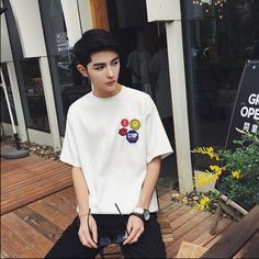 a young man sitting on a wooden bench in front of a building with yellow flowers