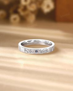 a white gold wedding band with an engraved design on the side, sitting on a wooden surface