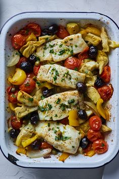 fish and vegetables in a casserole dish with tomatoes, olives, and parsley