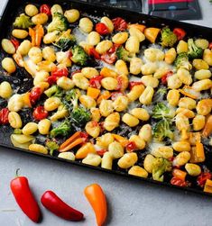 a tray filled with pasta and veggies on top of a table next to red peppers