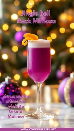 a purple drink with an orange slice on the rim in front of a christmas tree