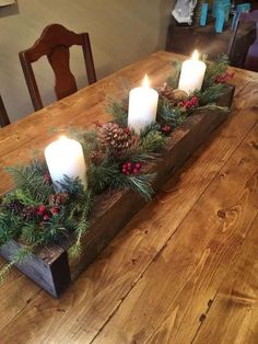 a wooden table topped with candles and greenery next to a candle holder filled with pine cones