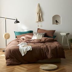 a bed with brown sheets and pillows in a white room next to a wooden floor