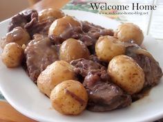 a white plate topped with meat and potatoes covered in gravy on top of a wooden table