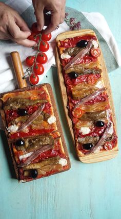 two rectangular shaped pizzas with tomatoes and olives on them, one being cut into slices