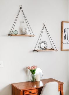 a desk and chair in a room with two shelves on the wall above it,