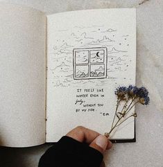 a hand holding a flower in front of an open book with writing on the pages