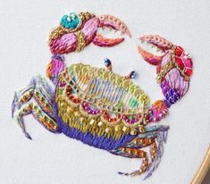 a colorful crab is embroidered onto a white piece of fabric with gold sequins