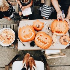 people are carving pumpkins with carved faces on them and sitting at a table outside