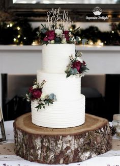 a three tiered cake with flowers on top is sitting on a tree stump in front of a fireplace