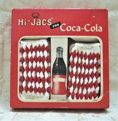 two red and white knitted socks with coca - cola bottle in the box on top