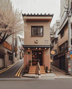 a woman walking down the street in front of a small building with stairs leading up to it