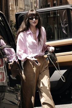 a woman in pink shirt and khaki pants stepping out of a black car