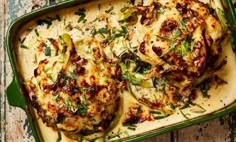 a green casserole dish with chicken and vegetables in it on a wooden table