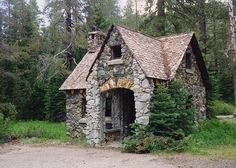 an old stone house in the middle of a forest with trees and bushes around it