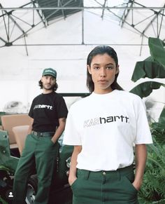 two people standing next to each other in front of plants