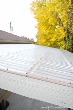 a white metal roof with some trees in the back ground and yellow leaves on it