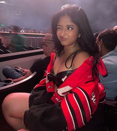 a woman in a red and black jacket sitting on a chair at a sporting event