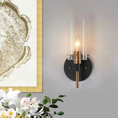 a wall mounted light next to a vase with flowers in it and a painting on the wall