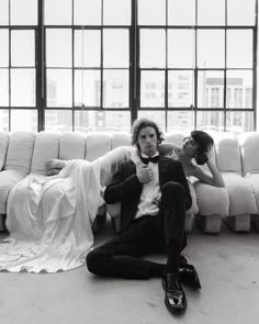 a man and woman laying on the floor in front of a white couch with large windows