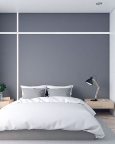 a bed with white sheets and pillows in front of a gray wall, next to a lamp