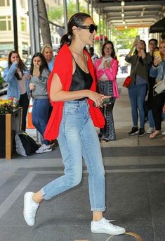 a woman is walking down the street while wearing sunglasses and a red cardigan jacket