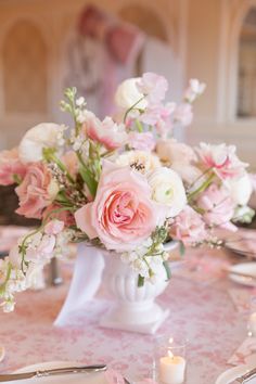 a white vase filled with pink and white flowers on top of a table covered in silverware