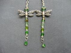 two green and silver dragonfly earrings on a gray surface with beads hanging from them