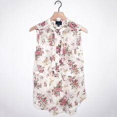 a white shirt with pink flowers on it hanging from a clothes hanger in front of a white wall