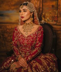 a woman sitting in a chair wearing a red and gold wedding dress with elaborate jewelry