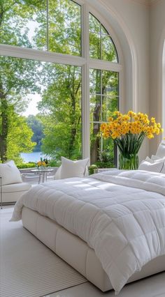 a large white bed sitting in a bedroom next to a window filled with yellow flowers